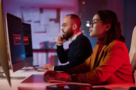 Side view portrait of computer programmers working in cybersecurity department with red emergency lights copy space - Powered by Adobe
