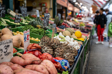 Vienna, Austria, August 23, 2022. At the Naschmarkt market, close-up shot with seasonal vegetables on display. Potatoes, shallots, garlic, green beans, artichokes. Blurred background with people.