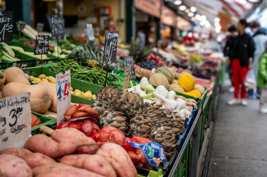 Vienna, Austria, August 23, 2022. At the Naschmarkt market, close-up shot with seasonal vegetables on display. Potatoes, shallots, garlic, green beans, artichokes. Blurred background with people.