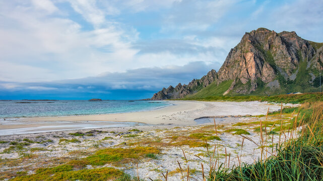 Beautiful Bleik Beach on And&oslash;ya Island with white sands, turquoise waters, and dramatic cliffs under a cloudy sky. Concept: nature, travel, serenity, scanic landscapes. Norway