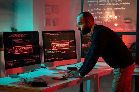 Side view portrait of adult cybersecurity expert working on emergency and using computer with critical error message on screen