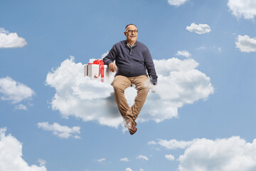 Happy mature man with a gift box sitting on a cloud