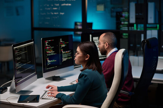High angle view at two people sitting at workplace in cybersecurity department and writing code in blue lights