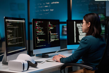 Female IT developer writing code for VR project at office workplace with focus on computer screens...