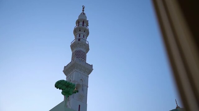 Traditional mosque minaret with mounted loudspeakers for the Islamic call to prayer (Adhan), featuring ornate architectural details against a clear blue sky. Ideal for themes of Islam, worship, faith,