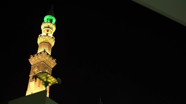 Night Traditional mosque minaret with mounted loudspeakers for the Islamic call to prayer (Adhan), featuring ornate architectural details against a clear blue sky. Ideal for themes of Islam, worship, 