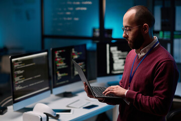 Side view portrait of bearded adult man as computer programmer holding open laptop in IT and...