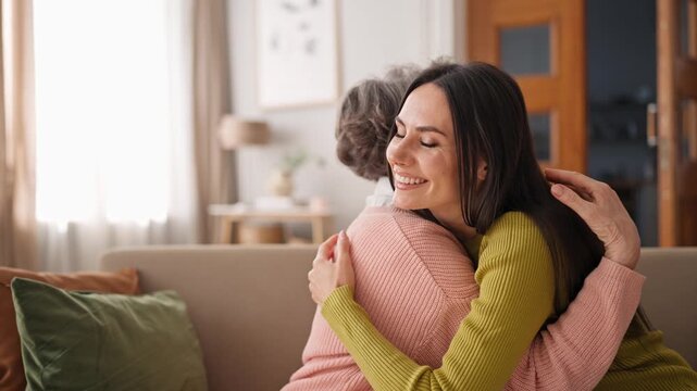 Happy Caucasian daughter hugging her mother tightly. Young girl clinging to mothers shoulder and embracing her with smile. Loving family enjoying moment of meeting after long separation.