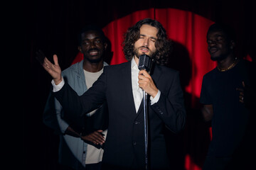 Professional jazz band, caucasian and african american mans pop music singers is performing song with retro microphone on stage with red curtains