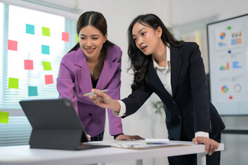 Two Businesswomen Collaborating on a Project in a Modern Office Setting with Digital Tablet and Sticky Notes