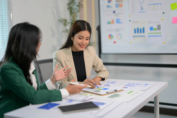 Businesswomen Discussing Financial Reports in Modern Office with Charts and Graphs on Whiteboard