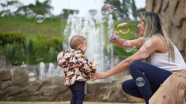 M&atilde;e assoprando bolhas de sab&atilde;o com seu filho pequeno em um parque 