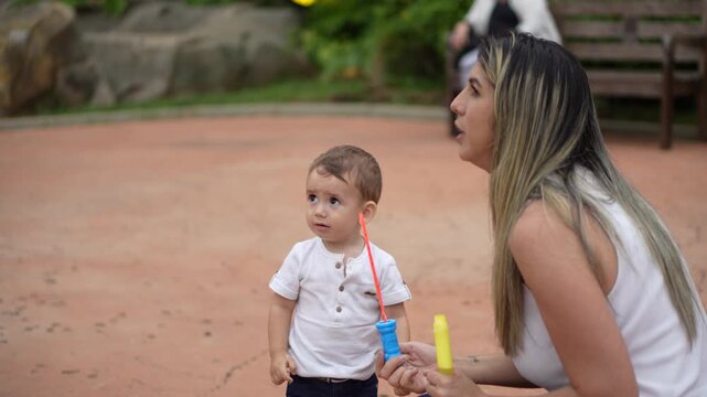 M&atilde;e assoprando bolhas de sab&atilde;o com seu filho pequeno em um parque 