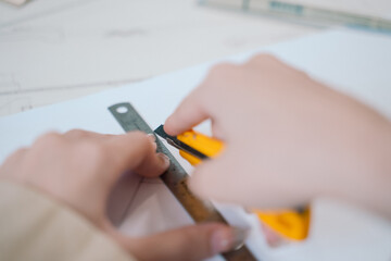 The teenage woman, working as a designer, deftly uses a cutter in her craft, meticulously drafting...