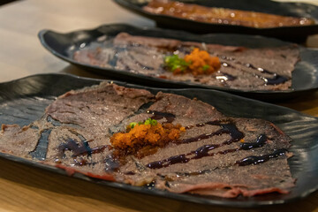 A delicious plate of thinly sliced beef with a side of dipping sauce.