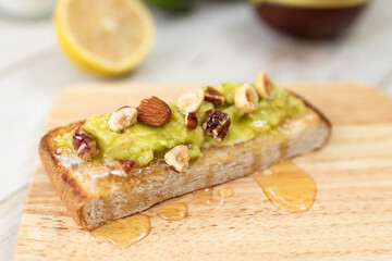 A delicious and healthy breakfast or lunch option. Avocado toast is made with fresh avocados, lemon, honey and topped with hazelnuts. It is served on a slice of whole wheat toast.