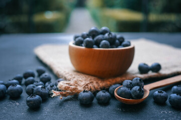 Wooden bowl filled with fresh blueberries and a wooden spoon with a few berries on a dark surface. The rustic presentation highlights the natural beauty and vibrant color of the fruit