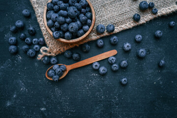 Wooden bowl filled with fresh blueberries and a wooden spoon with a few berries on a dark surface. The rustic presentation highlights the natural beauty and vibrant color of the fruit