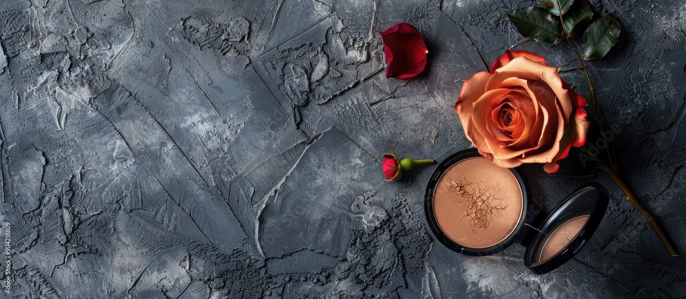 Aufkleber close up image with bronzer and rose flower placed on a textured grey surface providing empty space 