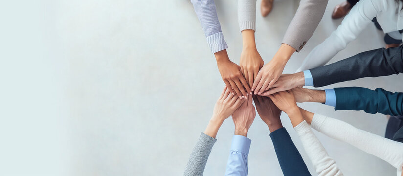 a diverse team of colleagues stands in a circle with their hands stacked in the center, symbolizing unity and teamwork. The background is a clean, bright office space with a minima