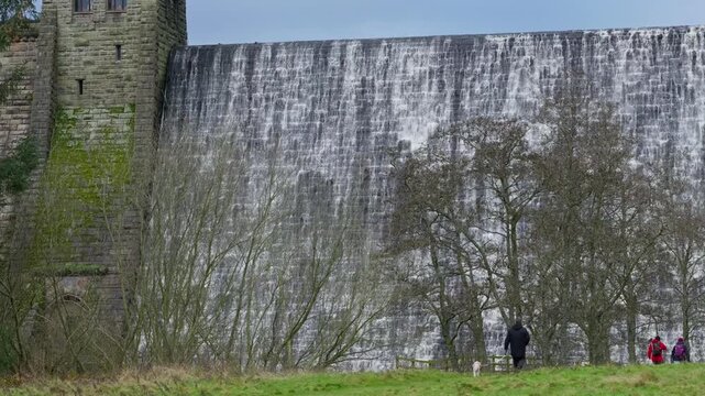 Young boy and woman and sightseers visiting the site of the Derwent Dam made famous in the Dam Busters movie. Showing water flowing over the dam. Winter scene shot outdoors in the UK