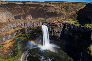 silky waters of Palouse Falls  flowing from the basalt canyon toward the Snake River with a rainbow on the side in Washington State