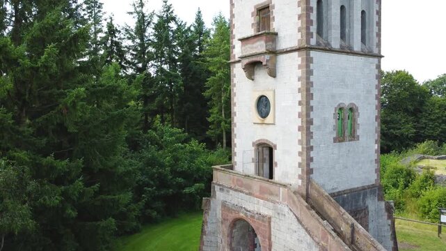 Drohnenflug auf historischen Turm zu mit bewaldeter Kulisse im Hintergrund