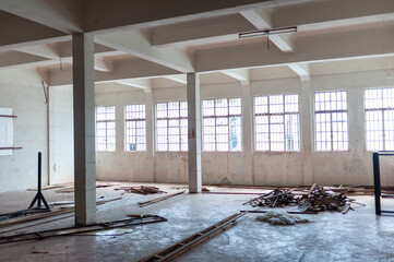 An empty room with large windows, debris on the floor, and exposed beams, ideal for renovation and...