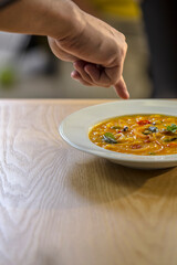 finger points at plate with indian dish dahl on wooden  table