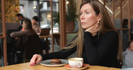 Sad lonely beautiful mid age woman sits with distant look alone in urban cafe. Young woman with long brown hair sitting in solitude at table with coffee and dessert in coffee shop. 4k footage.