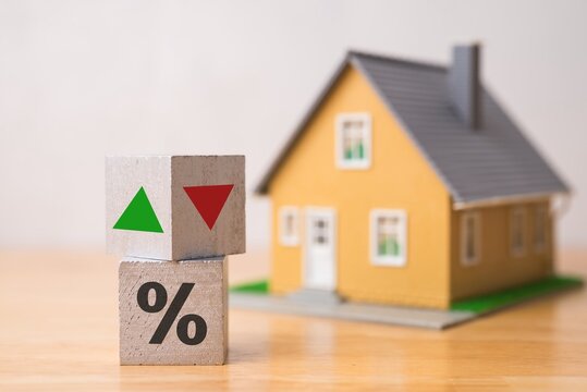 Wooden blocks percentage sign, arrow up and down with house model background. Central bank FED control interest rate increase or decrease effect to house price, monthly payment, buying home concept.