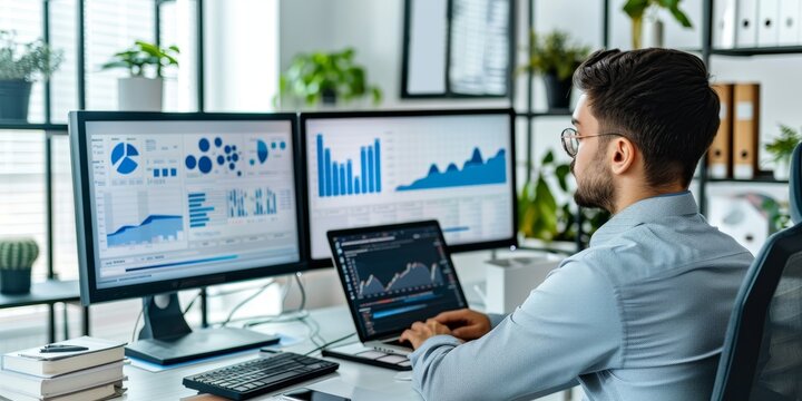 A professional in a modern office space, typing on a laptop, with multiple monitors displaying graphs and data analysis