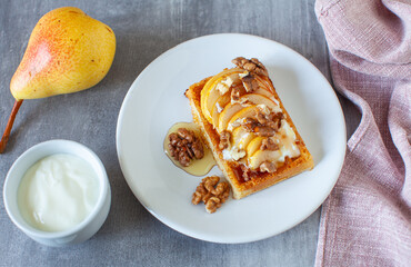 Autumn breakfast made by waffle, greek yogurt, pear with honey and walnuts topping