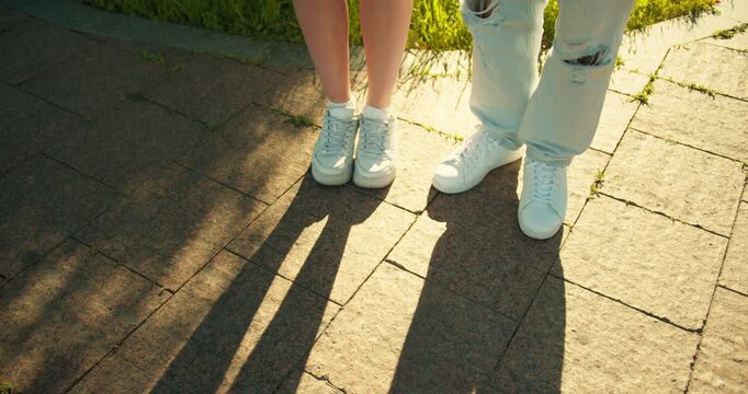 Close up the guy approaches the girl feet with his feet and stands next to her on the street on a sunny day
