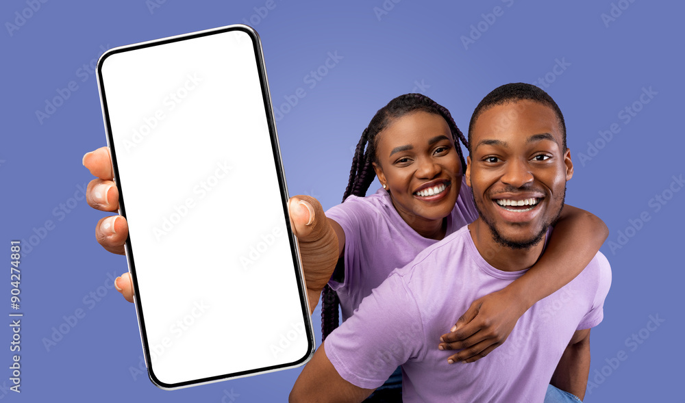 Poster A happy black couple poses for a picture while holding up a smartphone with a blank screen. They are both smiling and looking at the camera.