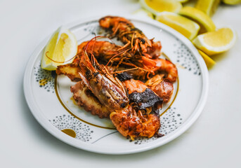 A plate with grilled shrimp and lemon slices on a white background