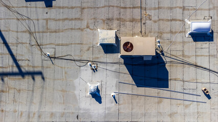 Aerial view of a flat commercial roof top with exhaust vents and air conditioning HVAC units. The roof shows signs of recent repair around the exhaust vent.