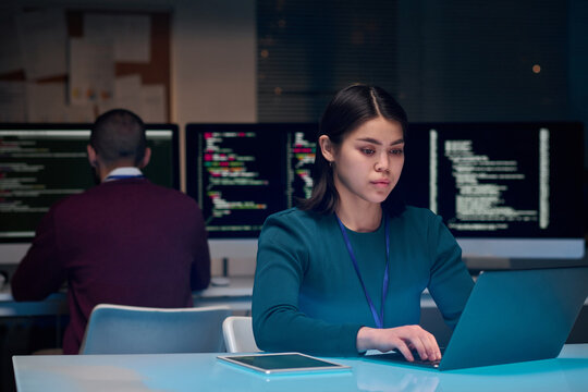 Portrait of young woman as software development expert using laptop at minimal office workplace with blue neon light copy space