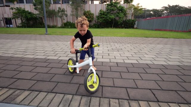 Little boy discovers broken limiter on his balance bike, allowing handlebars to spin freely. Concentrating, he demonstrates free rotation to us. Then, with excited and amazed look, he gazes upward