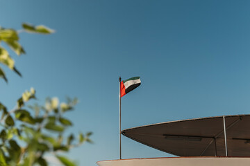 UAE flag waving in a clear blue sky with green blurred tree on the background