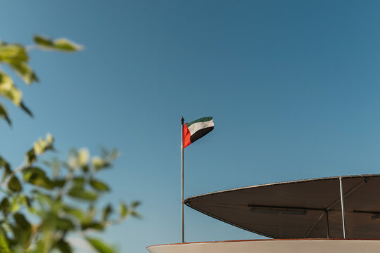 UAE flag waving in a clear blue sky with green blurred tree on the background