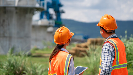 Survey team is working with a theodolite and road construction plans. Civil engineers are taking measurements with surveying tools during the construction.