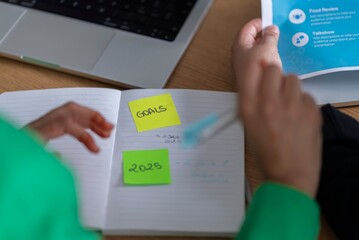 Close-up of a woman in hijab writing goals on sticky notes in a modern office setting, highlighting the importance of goal-setting for success.