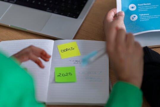 Close-up of a woman in hijab writing goals on sticky notes in a modern office setting, highlighting the importance of goal-setting for success.