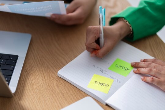 Close-up of a woman in hijab writing goals on sticky notes in a modern office setting, highlighting the importance of goal-setting for success.