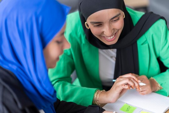 Woman in hijab focused on goal-oriented planning in a modern office, using notebooks and sticky notes to outline objectives and strategies.