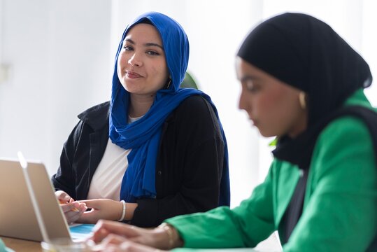 Two women in hijabs discussing their goals and strategies in a modern office, focusing on effective planning and collaboration.