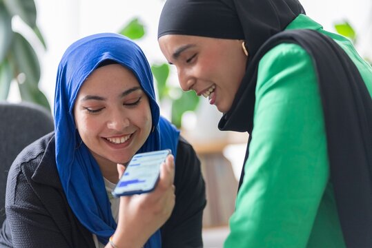 Two women in hijabs engaged in a goal-setting session in a modern office, using laptops and notes to outline their project goals.