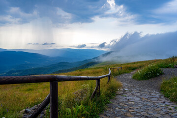Fototapeta premium Mountain trail and wooden barrier in Bieszczady at rainy summer day with torrential rian and moving clouds