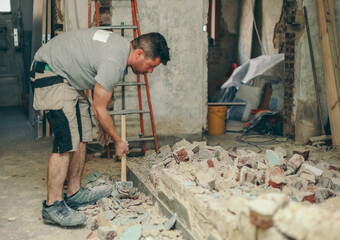A young man breaks a brick wall with a sledgehammer.